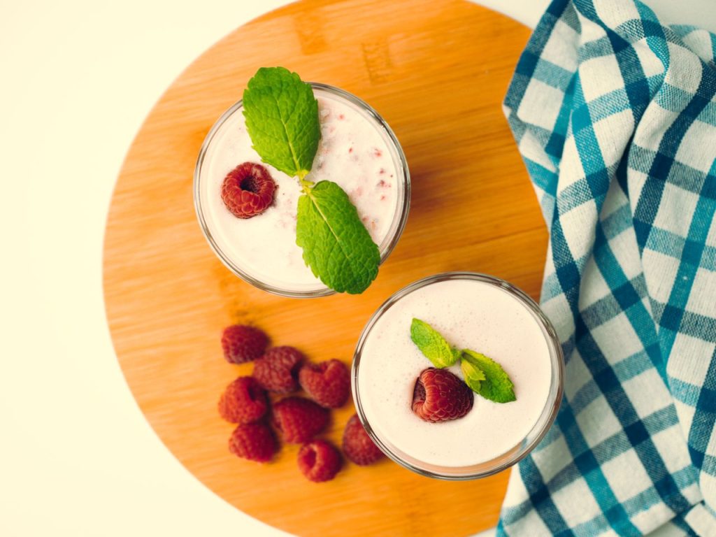 Top view of raspberry smoothies with mint leaves on a wooden board, perfect summer refreshment.