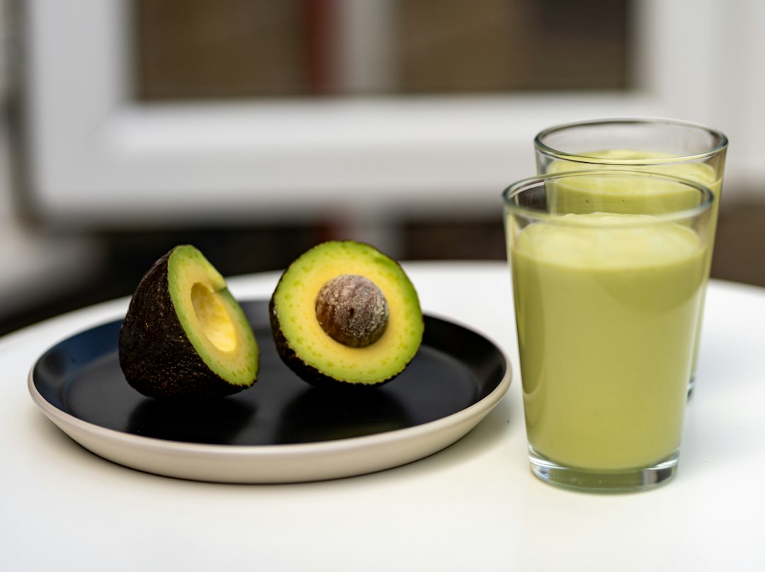 Glass of creamy avocado keto smoothie surrounded by fresh low-carb ingredients